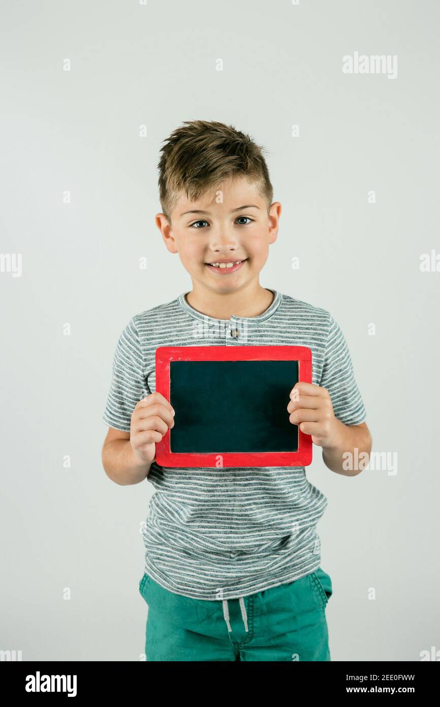 Pequeño chico sosteniendo un cartel rojo de pizarra en blanco con espacio para texto y un mensaje y espacio en blanco. Foto de stock