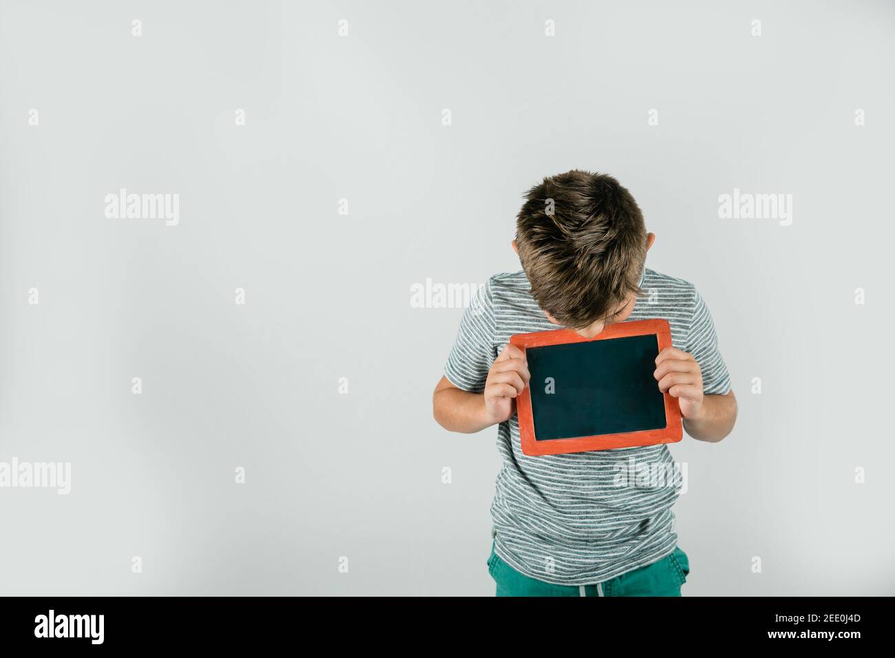 Pequeño chico sosteniendo un cartel rojo de pizarra en blanco con espacio para texto y un mensaje y espacio en blanco. Foto de stock