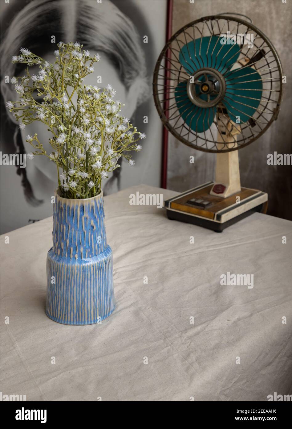 Ramo de flores blancas en jarrón azul de cerámica hecha a mano y.. antiguo  ventilador vintage sobre tela de mesa blanca texturizada en la parte  delantera De la película de póster chino