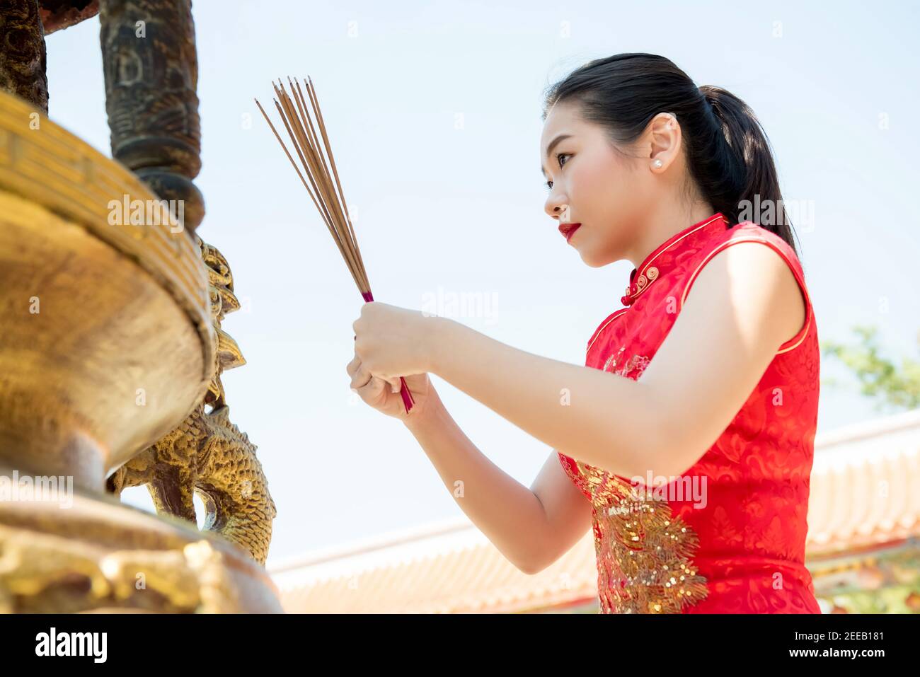 Mujer asiática en rojo vestido de qipao rezando con palos de incienso Durante el año Nuevo Chino o Lunar Foto de stock