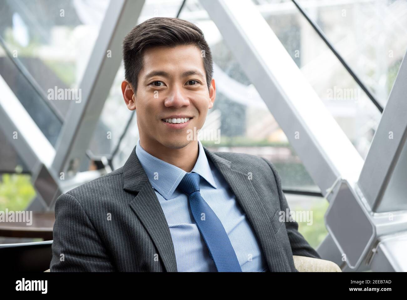 Joven y sonriente, un hombre de negocios asiático tailandés-chino sentado en el salón de la oficina Foto de stock