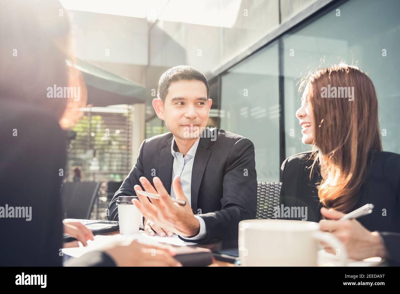 Un hermoso empresario asiático en una reunión, discutiendo el trabajo con su equipo y cliente en un café Foto de stock