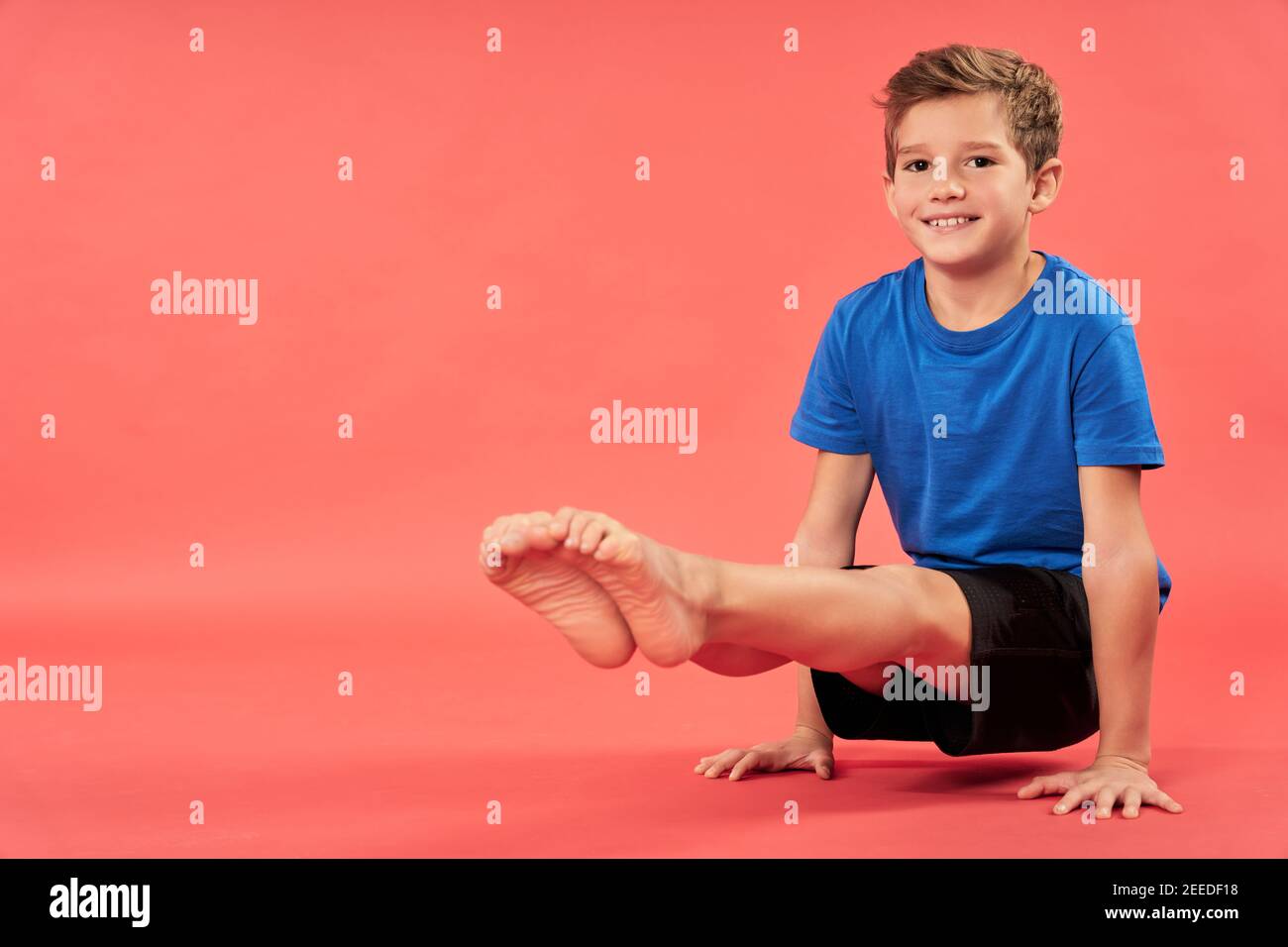 Adorable niño masculino en sportswear mirando cámara y sonriendo mientras se levanta y equilibra en dos manos Foto de stock