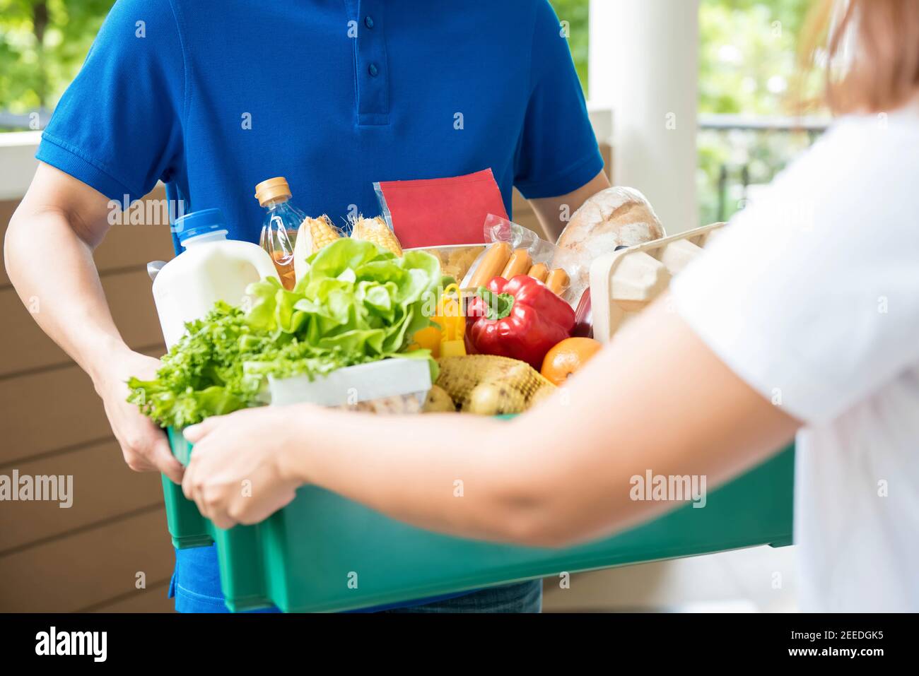 Un hombre de la entrega de la tienda de comestibles con un polo-camisa azul que entrega comida para una mujer en casa Foto de stock