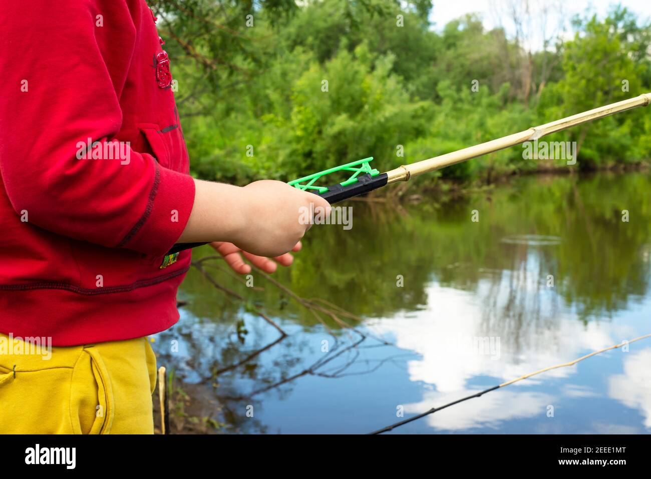 Las manos de los niños están sosteniendo una caña de pescar. Árboles verdes y un reservorio natural. Foto de stock
