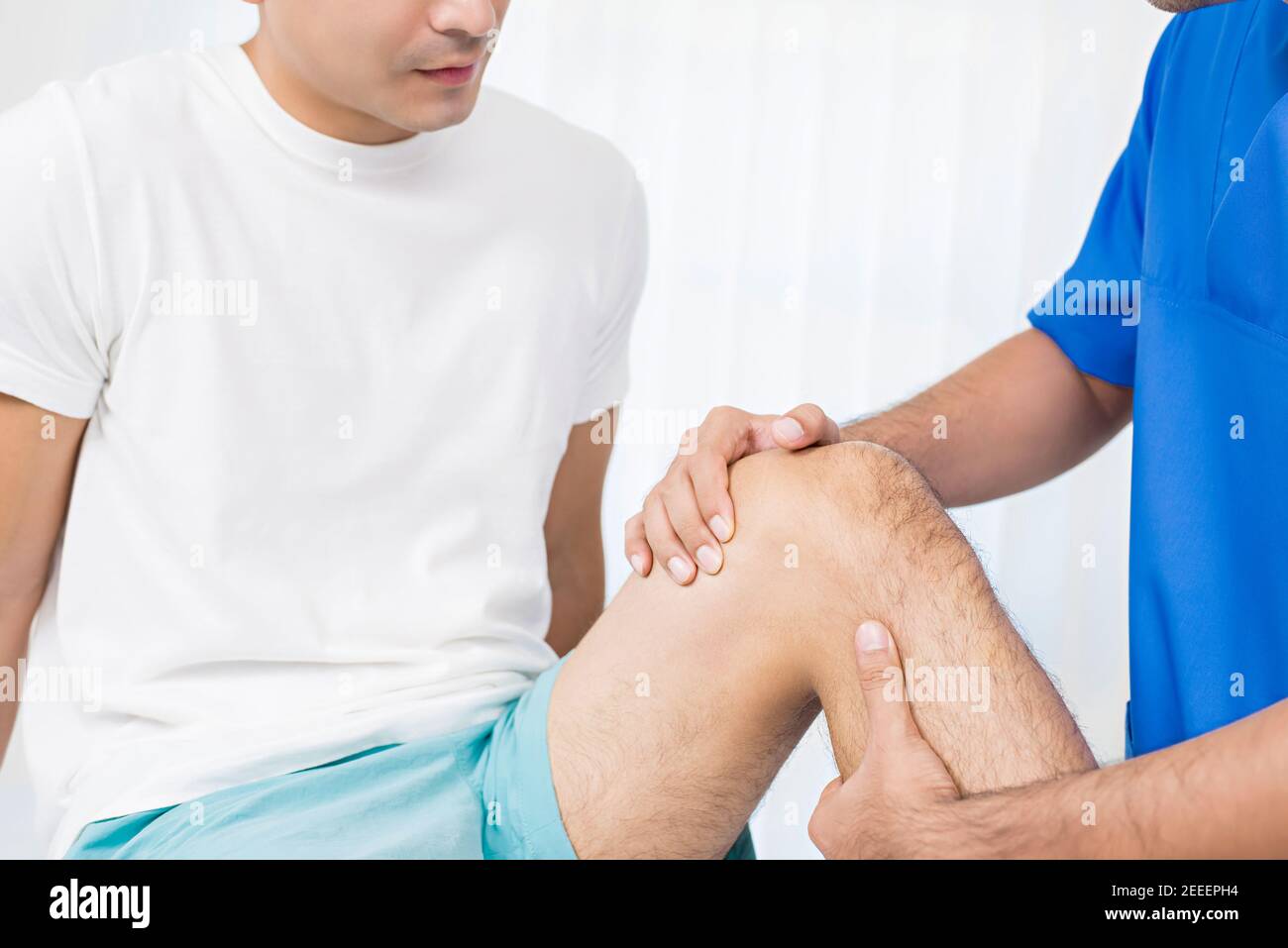Terapeuta que trata la rodilla lesionada del paciente masculino en el hospital - concepto de fisioterapia Foto de stock