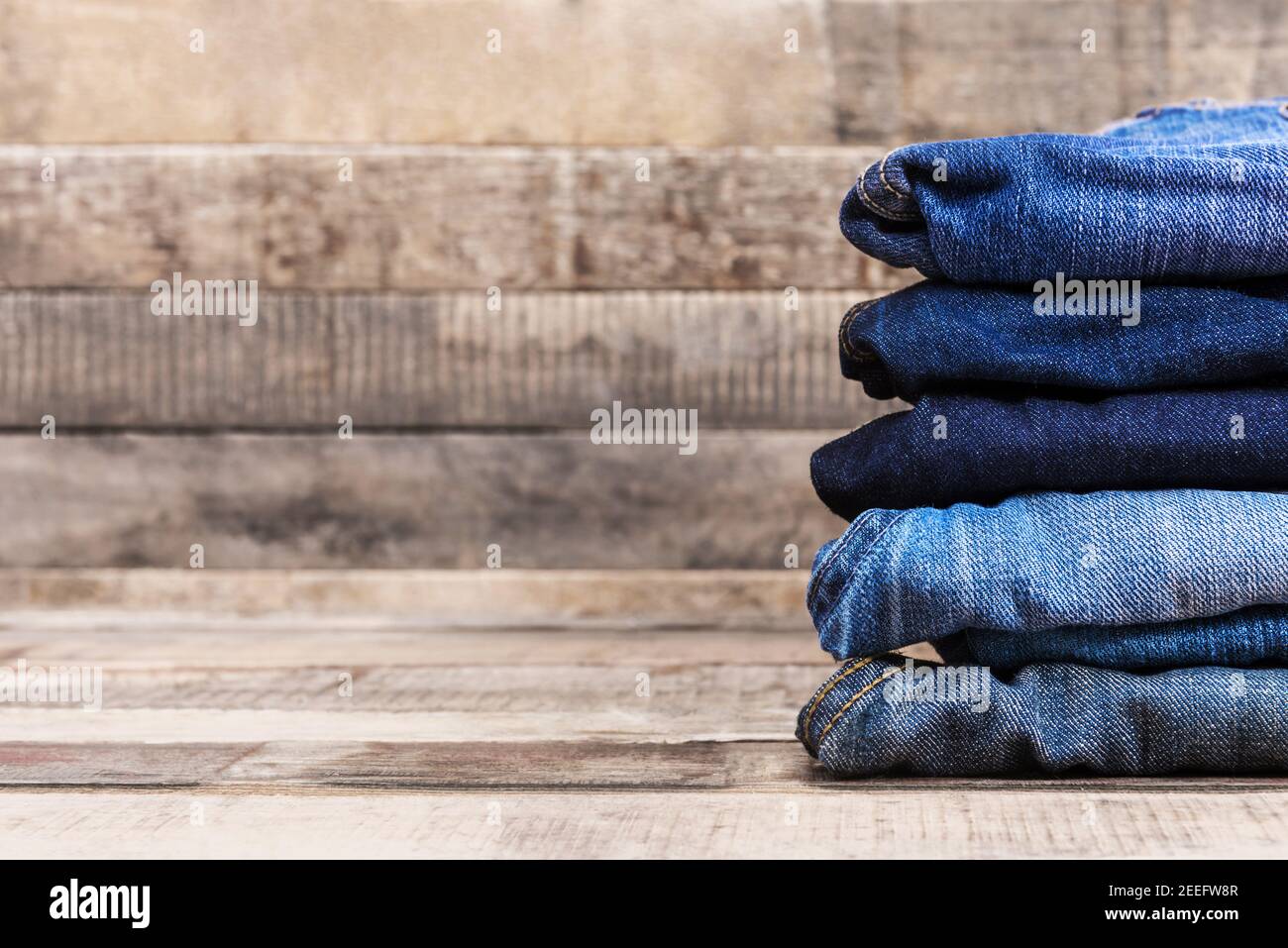 Pila de jeans azules plegados sobre fondo de madera vieja con espacio de copia Foto de stock