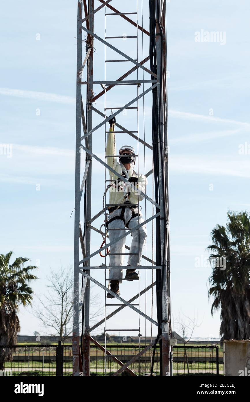 Concepto: Trabajo vertical. Hombre con traje de nbc, arnés, casco y equipo para la altura. una torre de metal de antenas con ganchos Fotografía de stock - Alamy