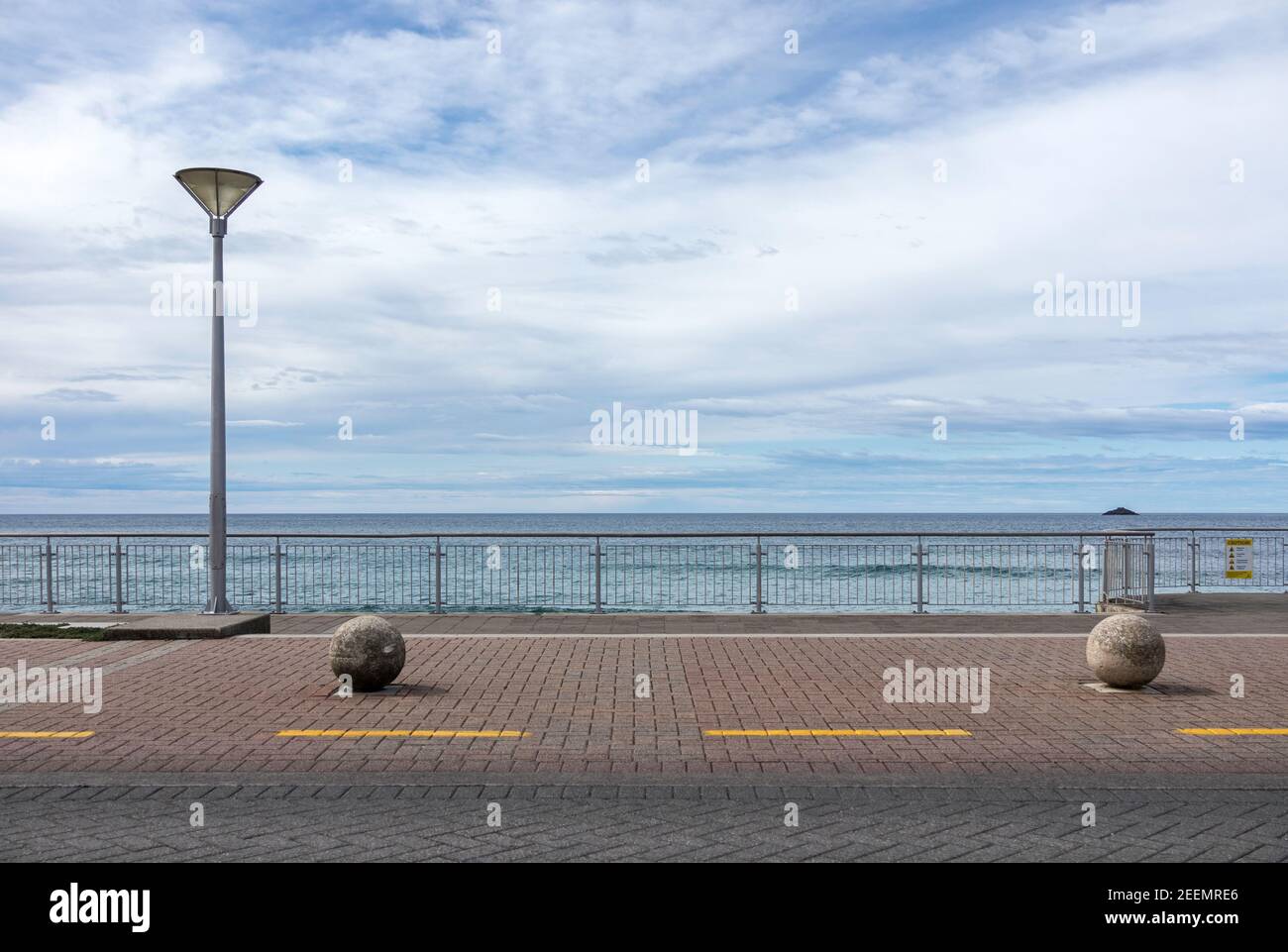 Esplanade en St Clair, Dunedin, Nueva Zelanda con un solo poste de luz y 2 bolardos esféricos de hormigón contra un fondo de mar y cielo azul, copyspace Foto de stock