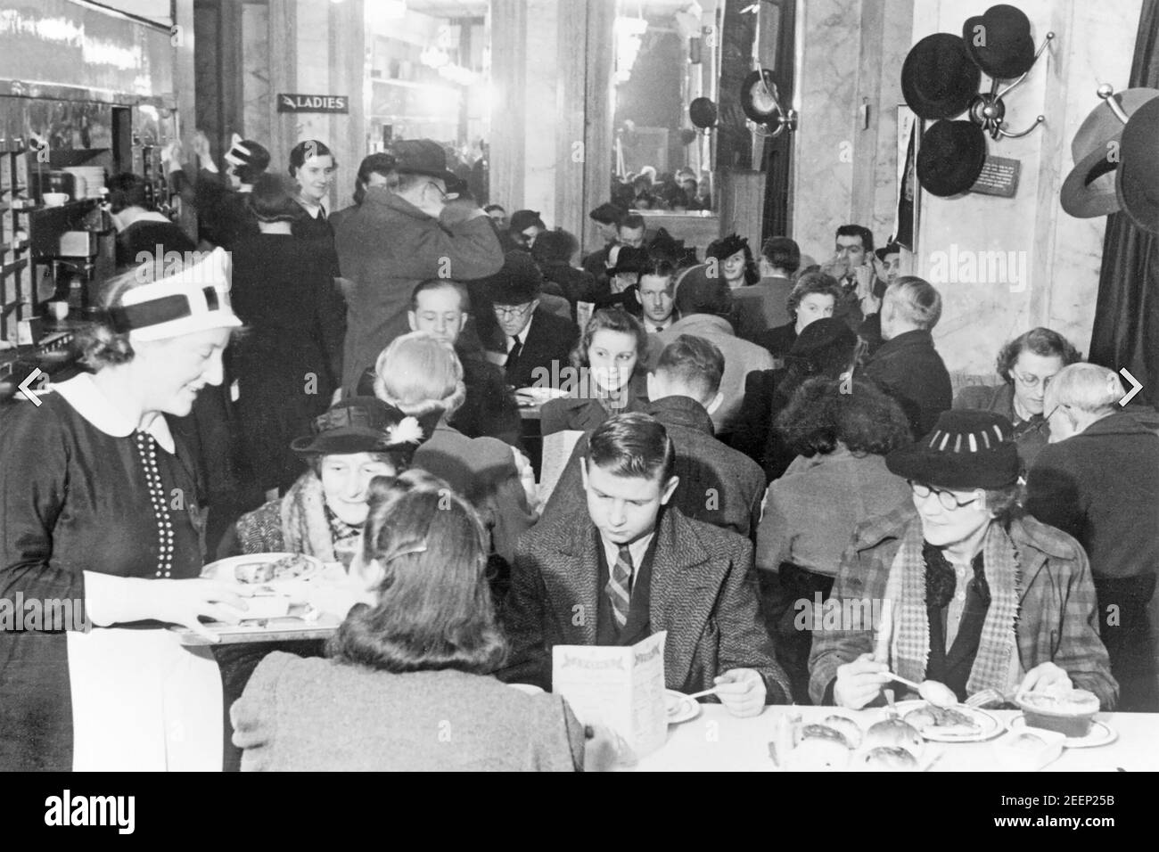 J. LYONS & CO cadena de restaurantes, restaurantes y hoteles británica fundada en 1884. Los clientes empacados para el té de la tarde en la famosa Lyons' Corner House en Coventry Street, Londres en enero de 1942. Una de las famosas camareras de Nippie está haciendo el servicio. Foto de stock