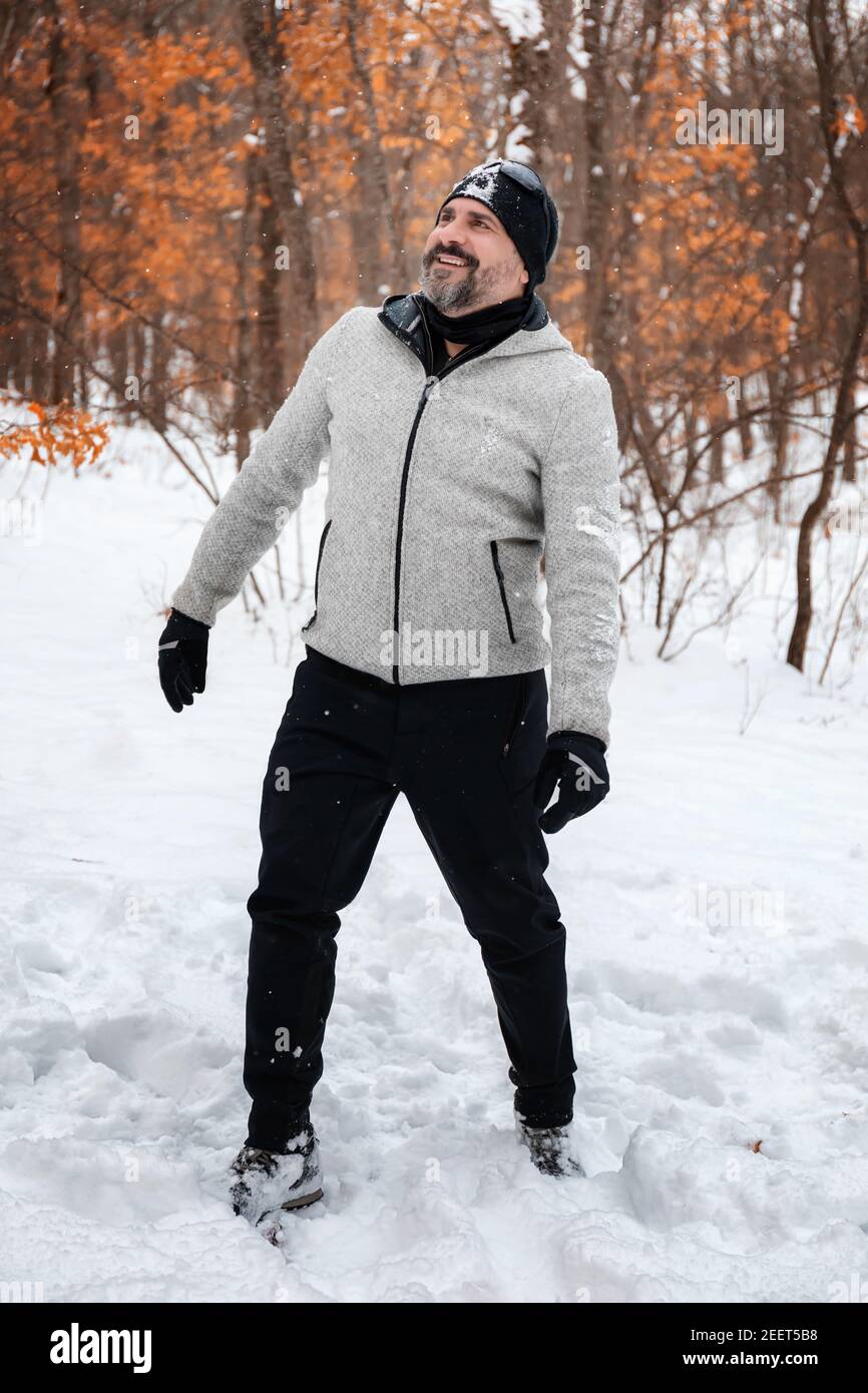 Un hombre barbudo con ropa de montaña, sudaderas grises, guantes y sombrero  negro, inmerso en el bosque nevado, se regocija por los copos de nieve que  caen Fotografía de stock - Alamy