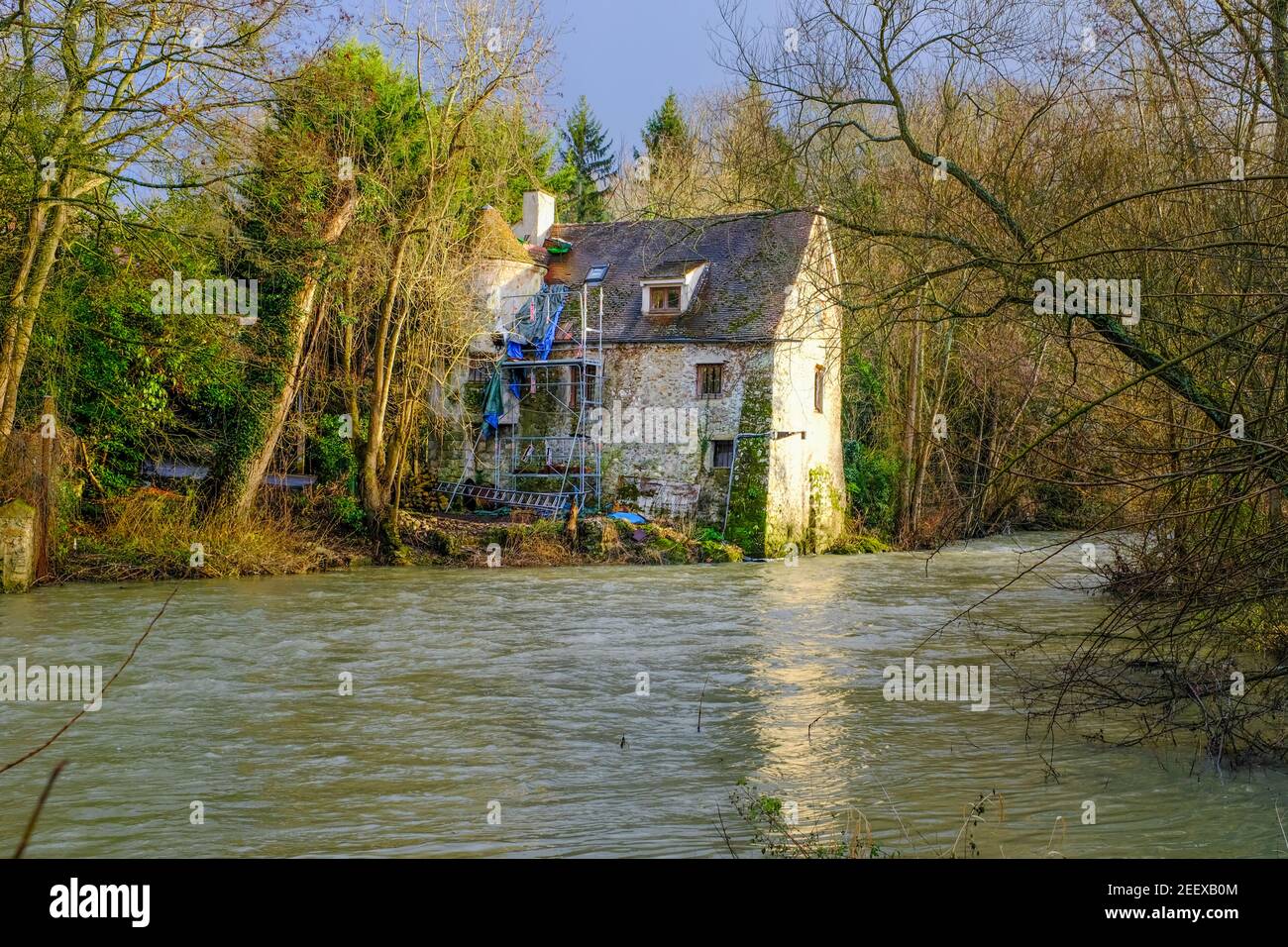 Antiguo molino de piedra en el borde de un pequeño río. Tomado de lejos en un soleado día de invierno cerca de París, Francia Foto de stock