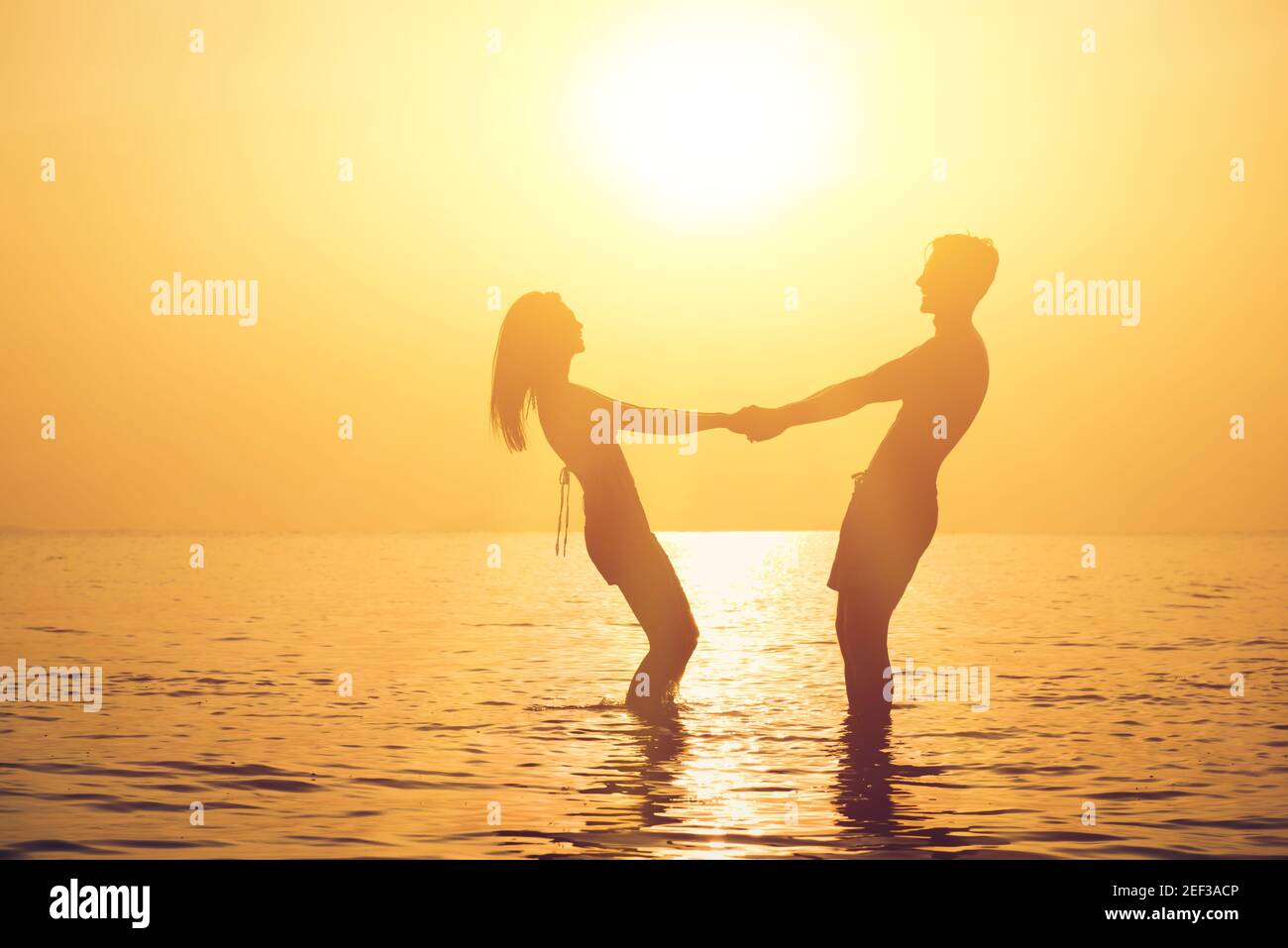 Silueta de pareja romántica que sostiene las manos en la playa en puesta de sol al atardecer Foto de stock