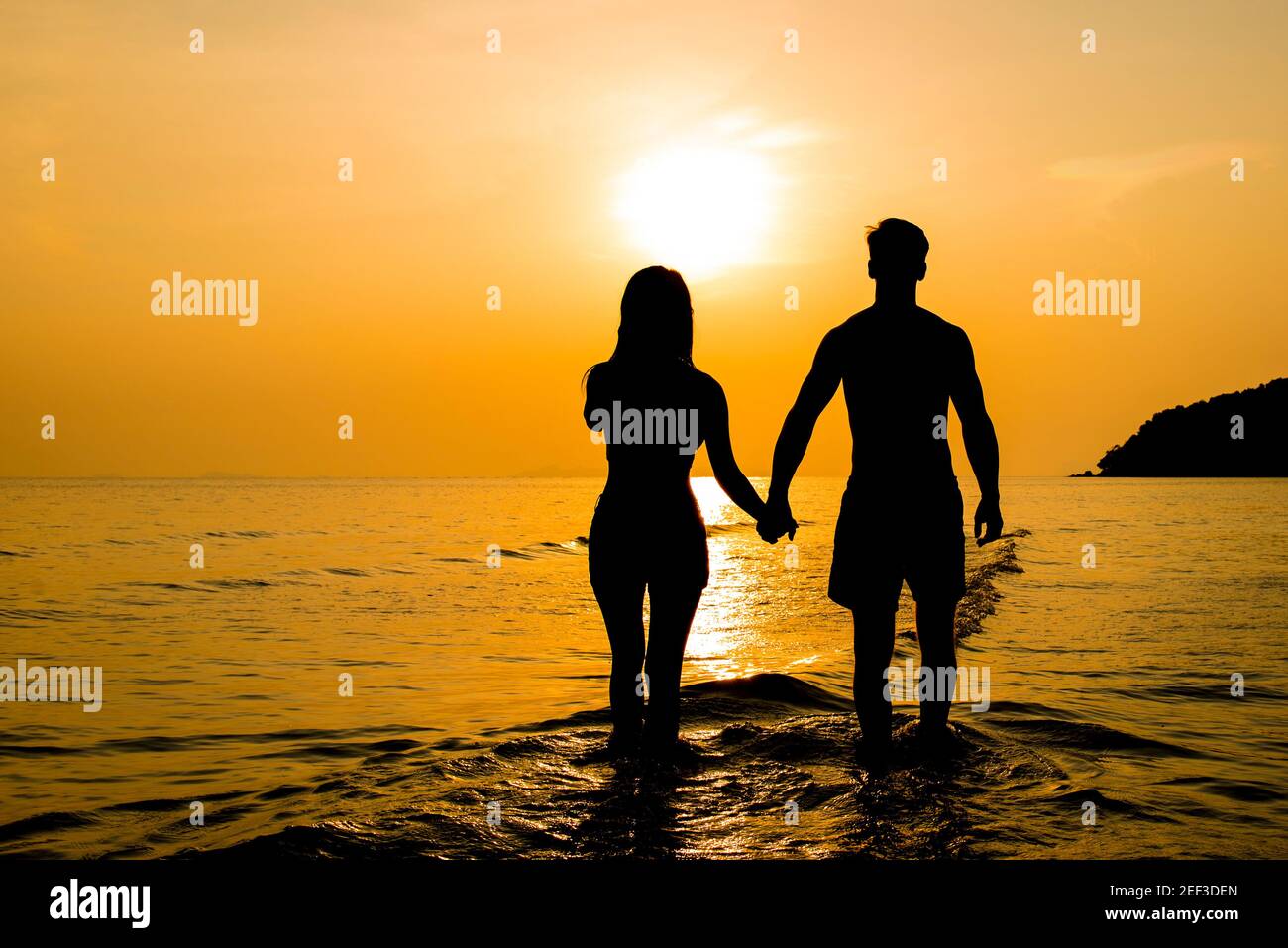 Silueta de pareja que sostiene las manos en la playa al atardecer Foto de stock