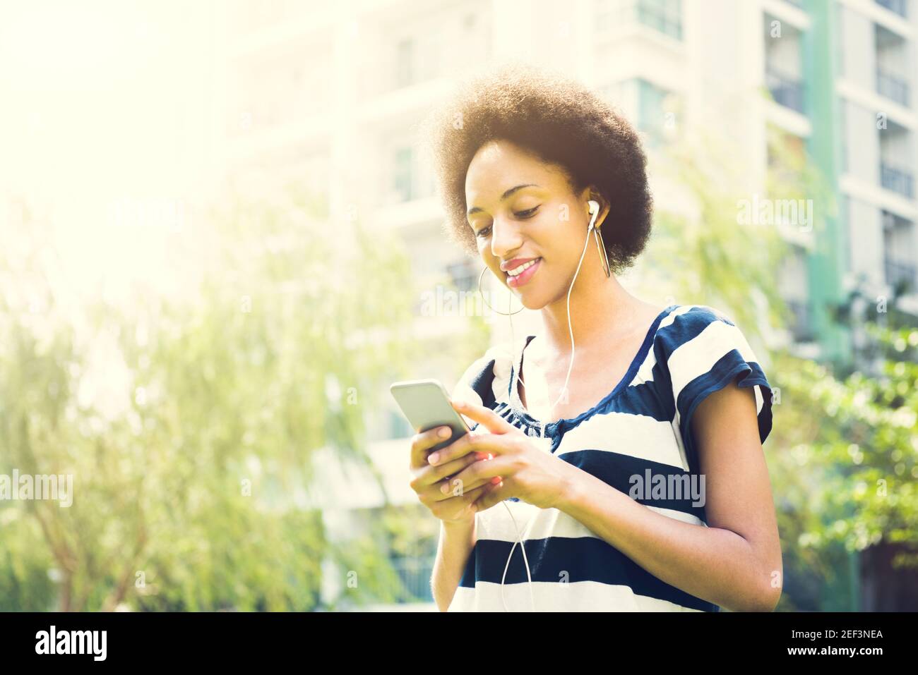 Joven mujer afro con auriculares escuchando música desde un smartphone en el parque Foto de stock