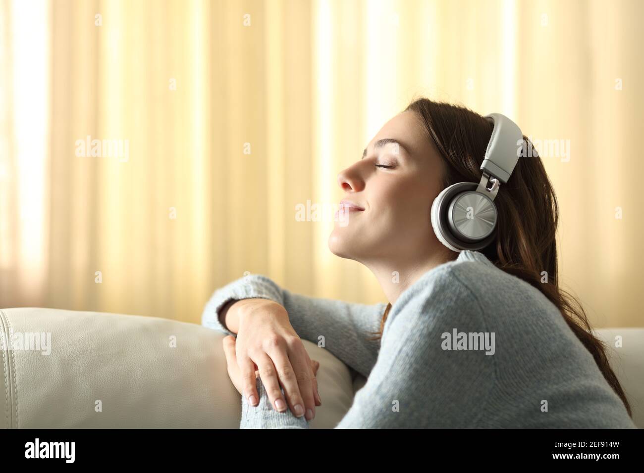 Perfil de una mujer respirando escuchando música con auriculares en un sofá en casa Foto de stock