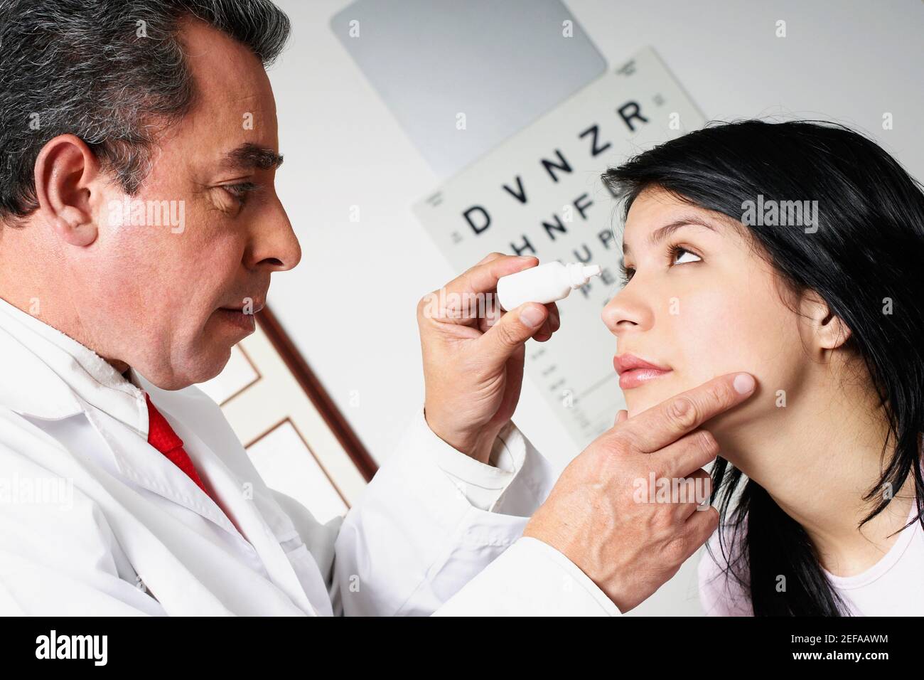 Perfil lateral de un médico masculino que pone gotas para los ojos Un ojo womanŽs joven Foto de stock