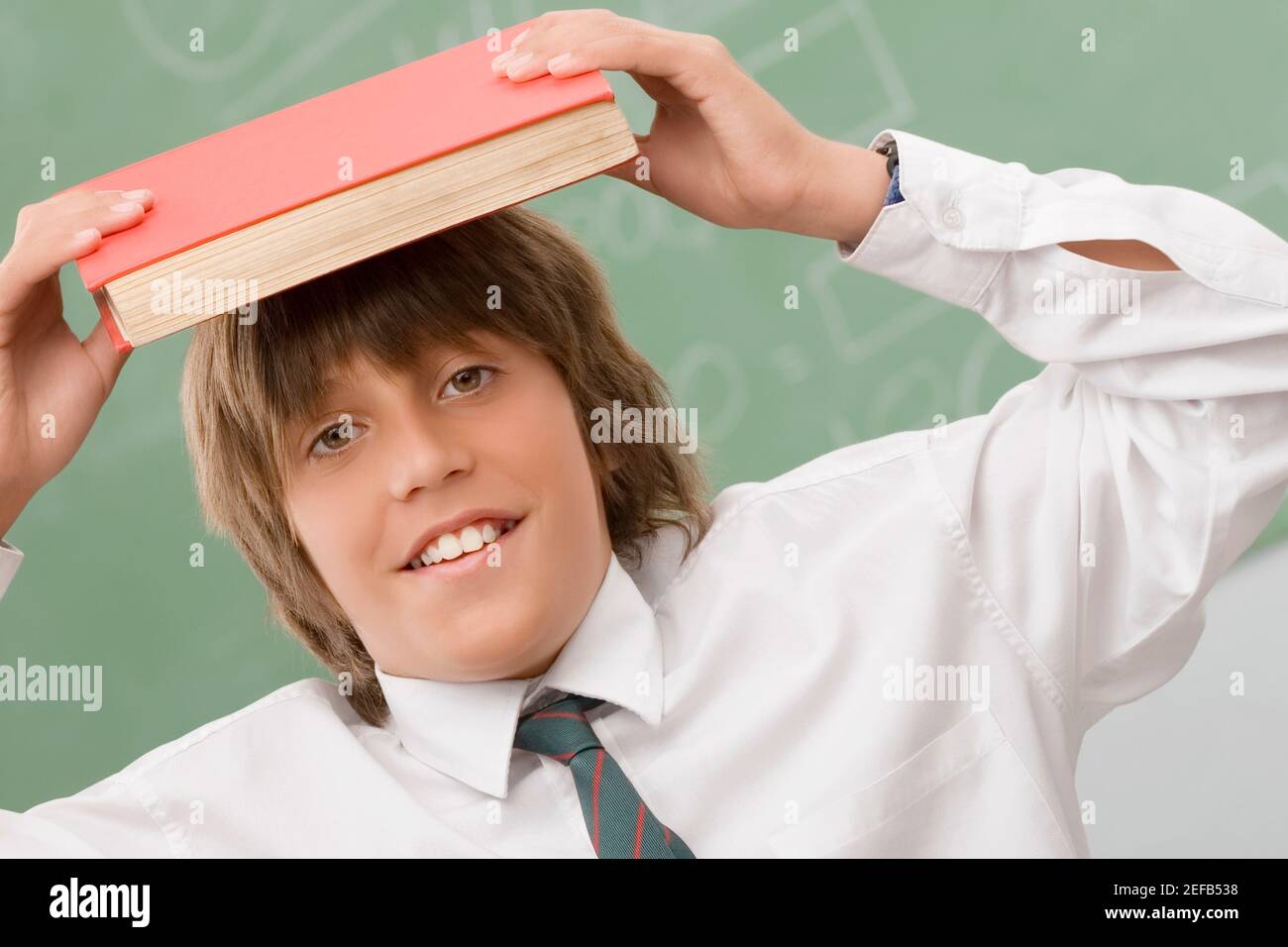 Retrato de un niño que sostiene un libro sobre su cabeza y sonriendo Foto de stock