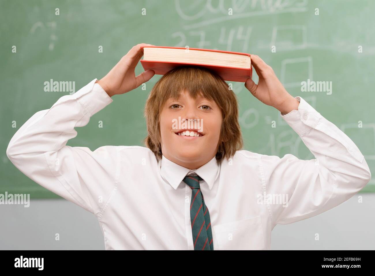 Retrato de un niño que sostiene un libro sobre su cabeza y sonriendo Foto de stock