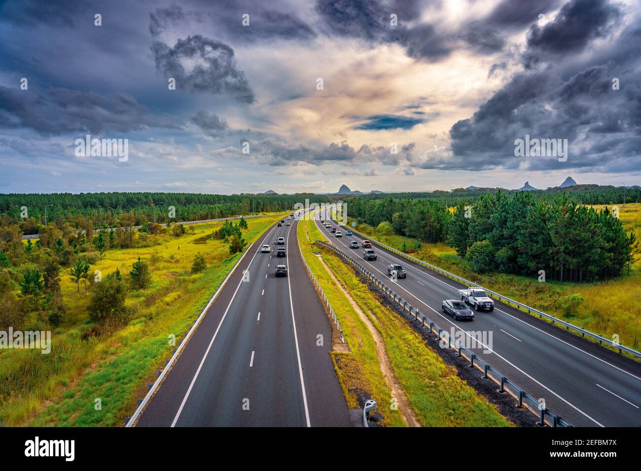 Queensland, Australia - Autos que se mueven a lo largo de Bruce Hwy con las montañas Glass House en el fondo Foto de stock