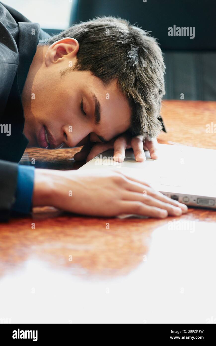 Perfil lateral de un hombre de negocios descansando su cabeza en un escritorio frente a un ordenador portátil Foto de stock