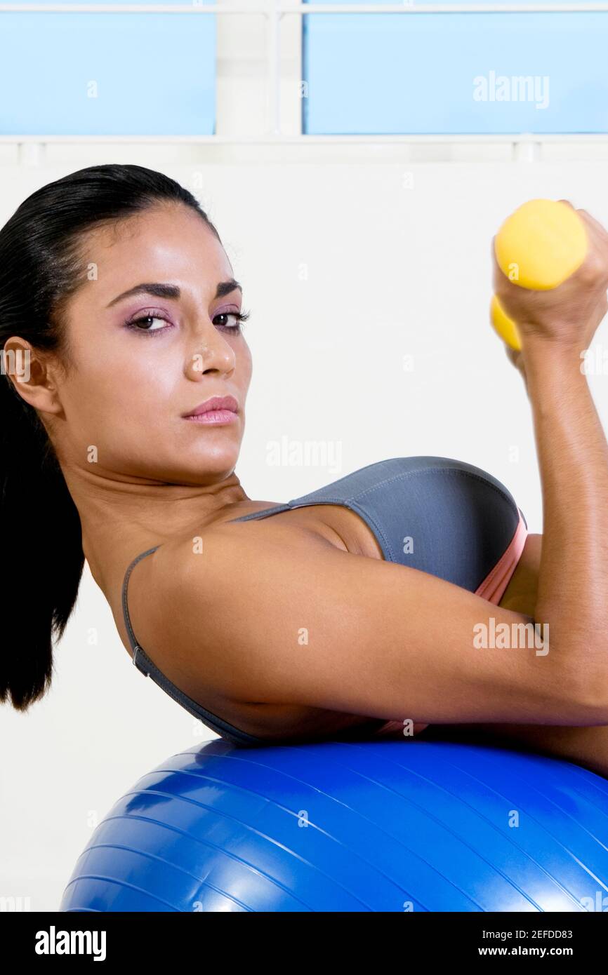 Retrato de una mujer joven haciendo ejercicio con pesas en un pelota de fitness Foto de stock