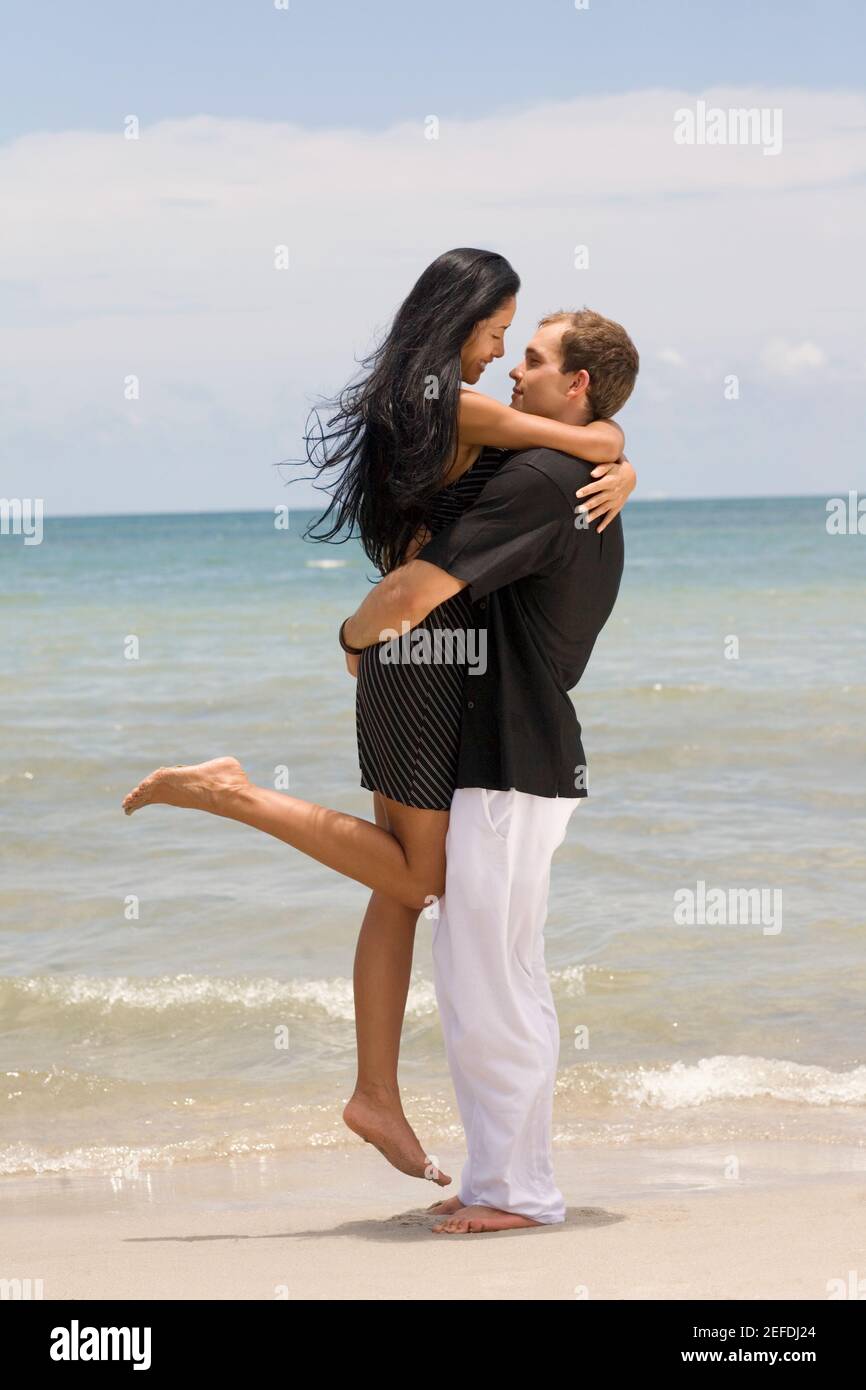 El perfil lateral de una joven pareja abrazándose entre otros en la playa Foto de stock
