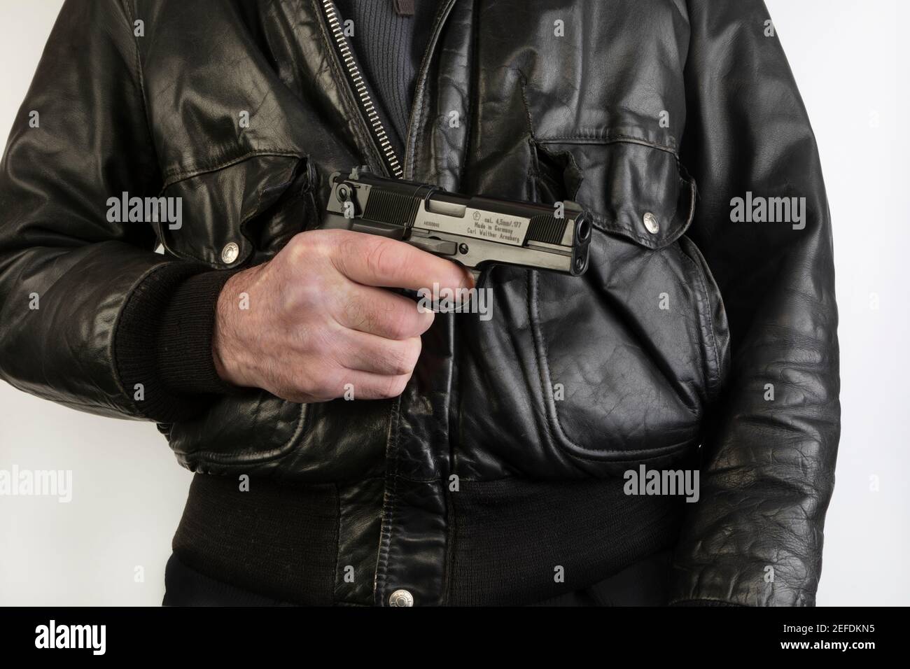 Un hombre en una chaqueta de cuero negro que sostiene una Walther P88 réplica de pistola de aire Foto de stock