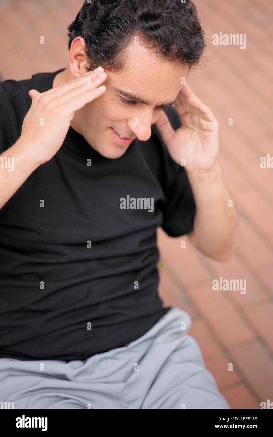 Primer plano de un joven haciendo sentadas y tocando la suya templos Foto de stock