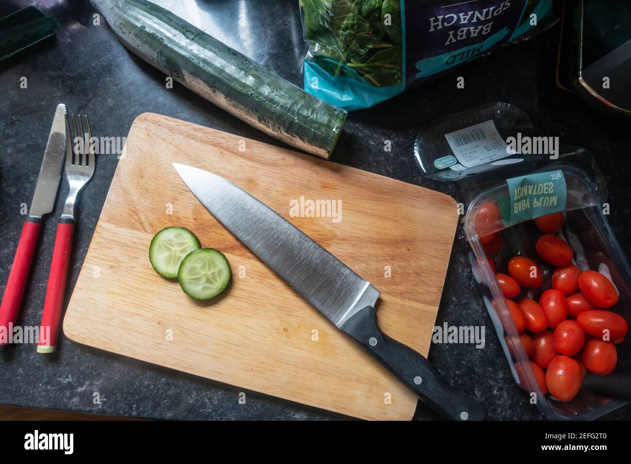 Mirando hacia abajo un cuchillo de cocina en una tabla de madera en una encimera de cocina lista para preparar un poco de comida. Foto de stock