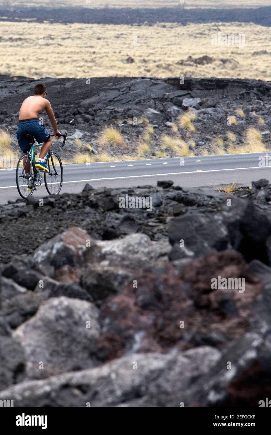 Vista trasera de un hombre montando en bicicleta por la carretera, Kona Coast, Big Island, Hawaii Islands, Estados Unidos Foto de stock