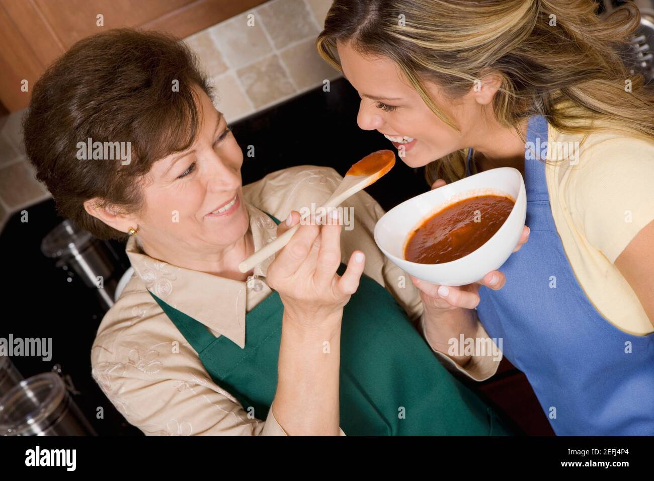 Mujer mayor alimentando sopa de tomate a su hija en el cocina Foto de stock