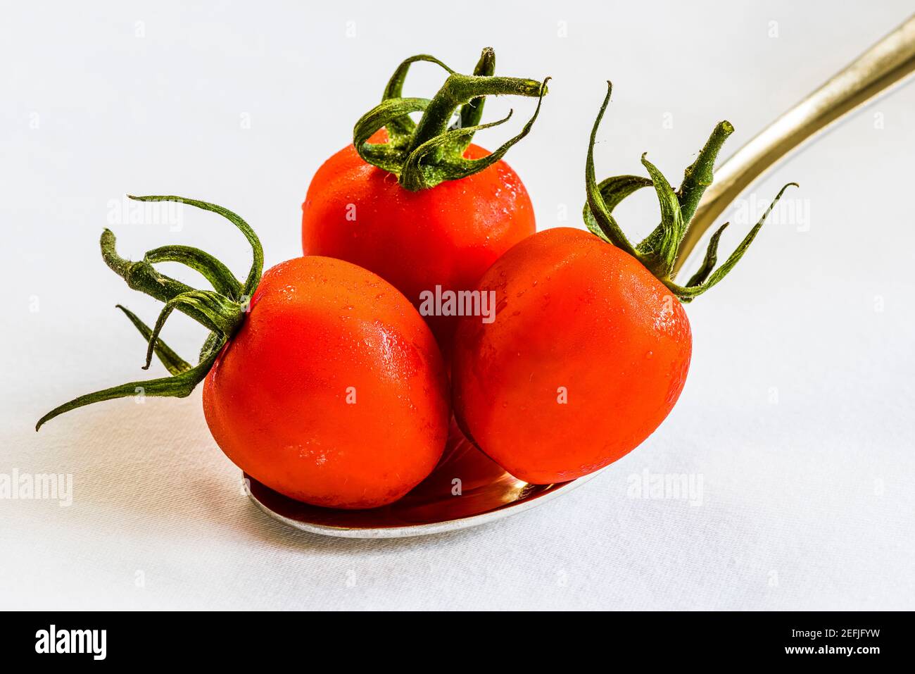 Primer plano de tres tomates rojos en una cuchara sobre un mantel blanco, Londres, Reino Unido Foto de stock