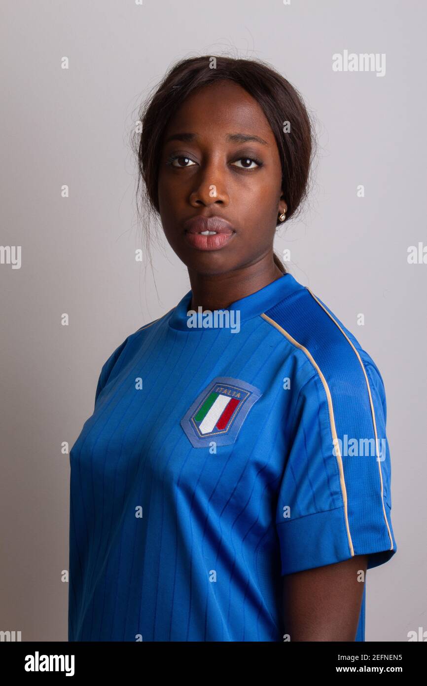 Hermosa chica afro italiana con la camiseta del equipo nacional de fútbol italiano. Modelo aislado sobre fondo gris. Foto de stock