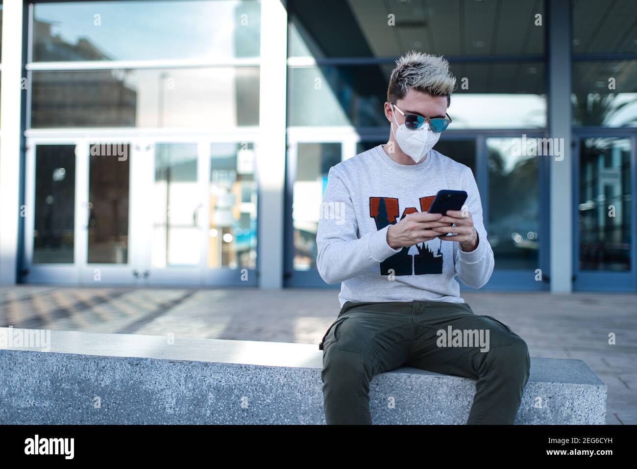 Joven tipo fresco con pelo corto de hombre usando un sanitario máscara y  gafas de sol usando su teléfono Fotografía de stock - Alamy