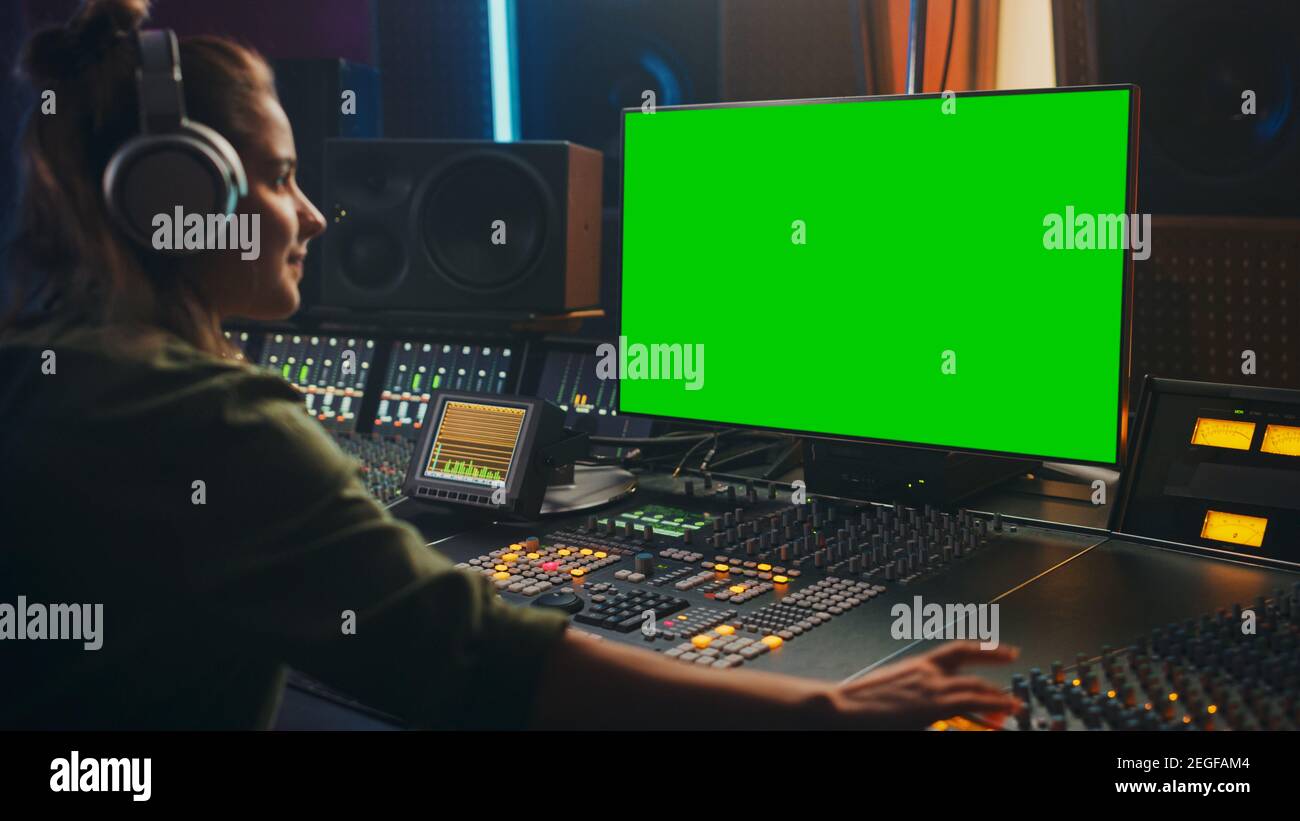 Elegante Audio Ingeniero productora trabajando en Music Record Studio, utiliza auriculares, pantalla verde de ordenador, placa mezcladora, escritorio de control a. Foto de stock