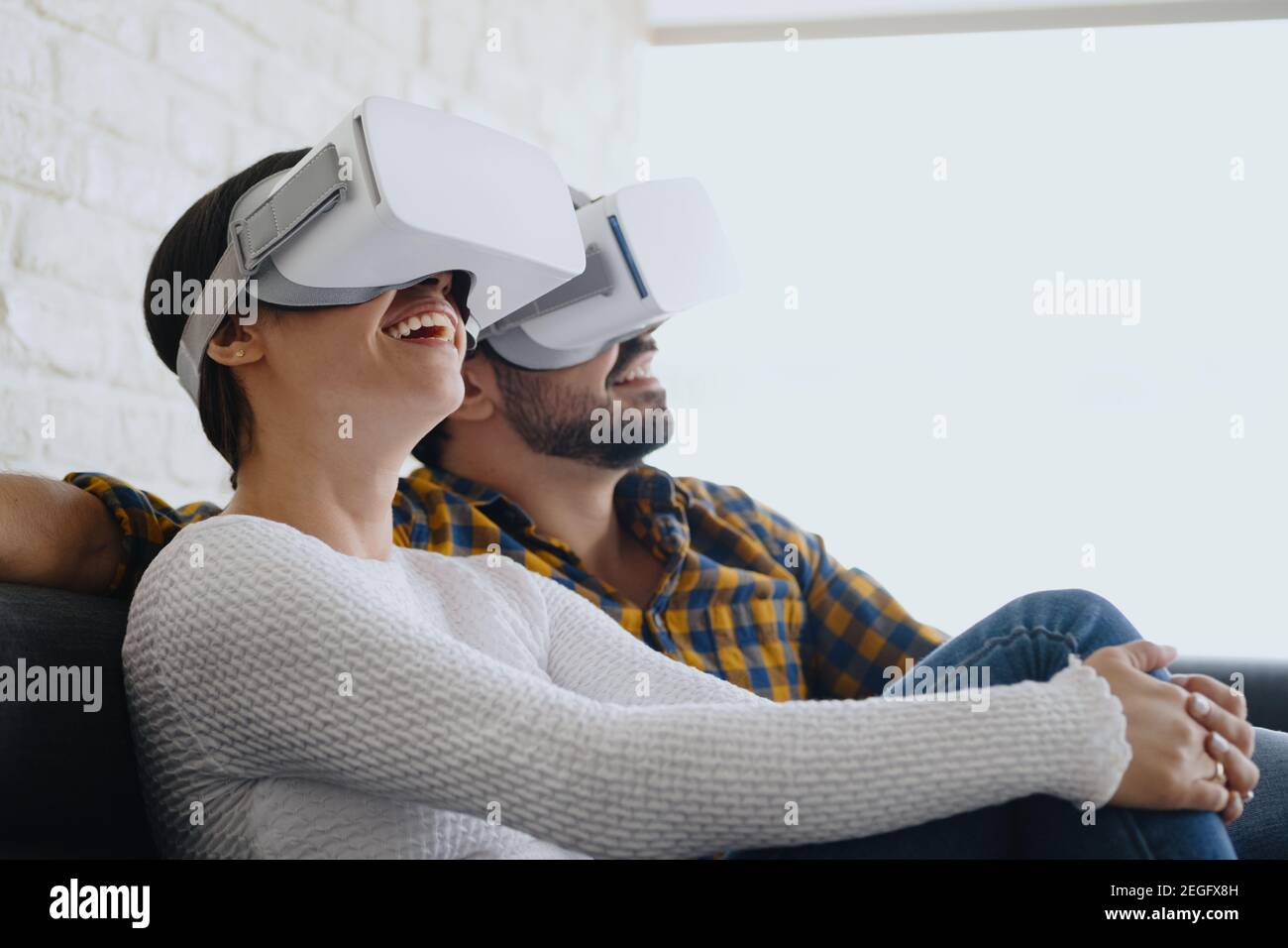 Pareja joven jugando a la realidad Virtual con auriculares en el sofá Foto de stock