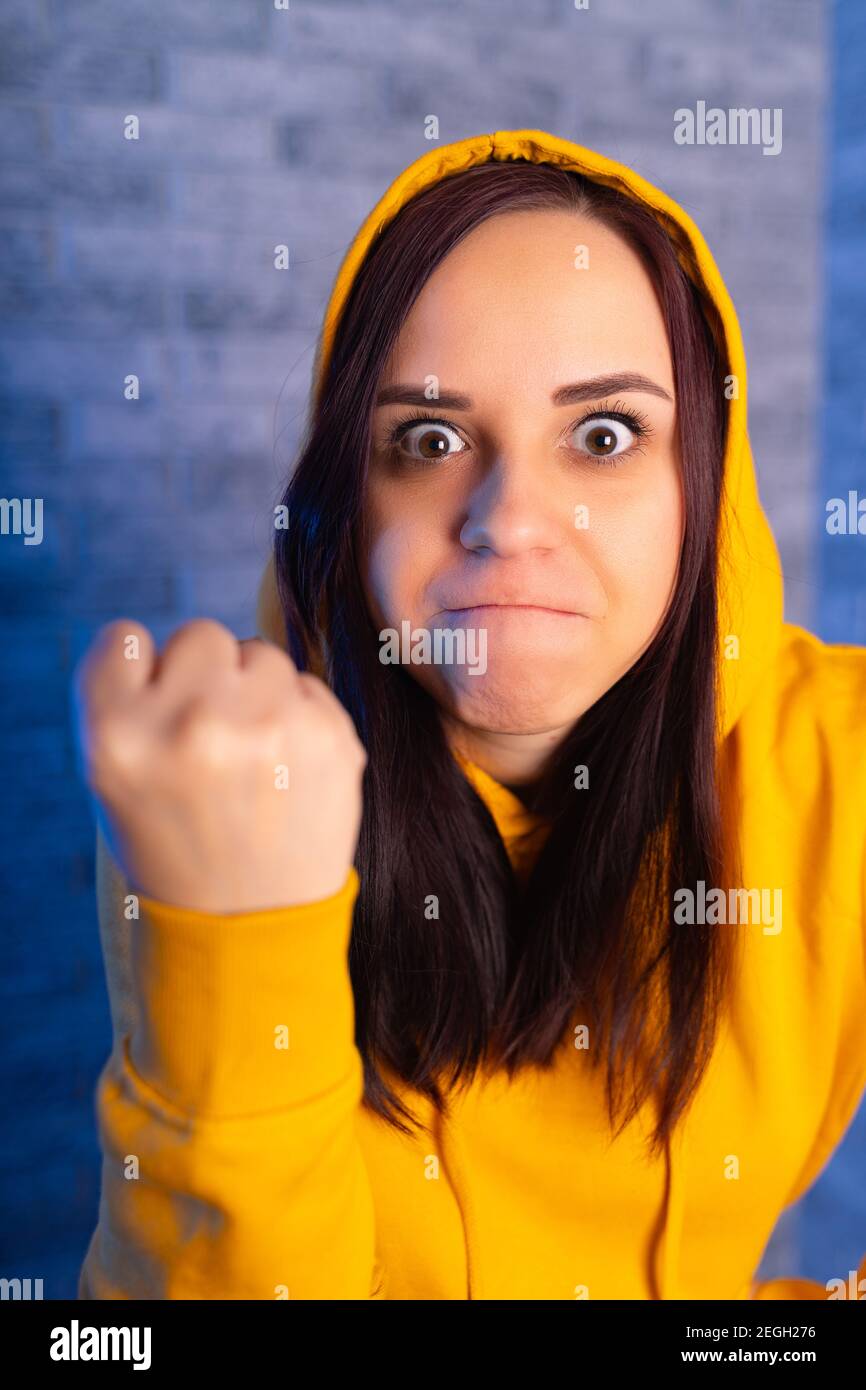 Retrato de una joven insatisfecha mostrando el puño. El primer plano de la hembra en color amarillo muestra el puño, mirando la cámara Foto de stock