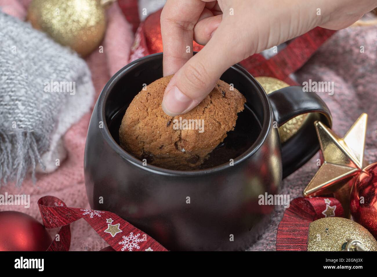 Sumergir la galleta de jengibre en la bebida en la mesa cubierta con adornos de navidad Foto de stock