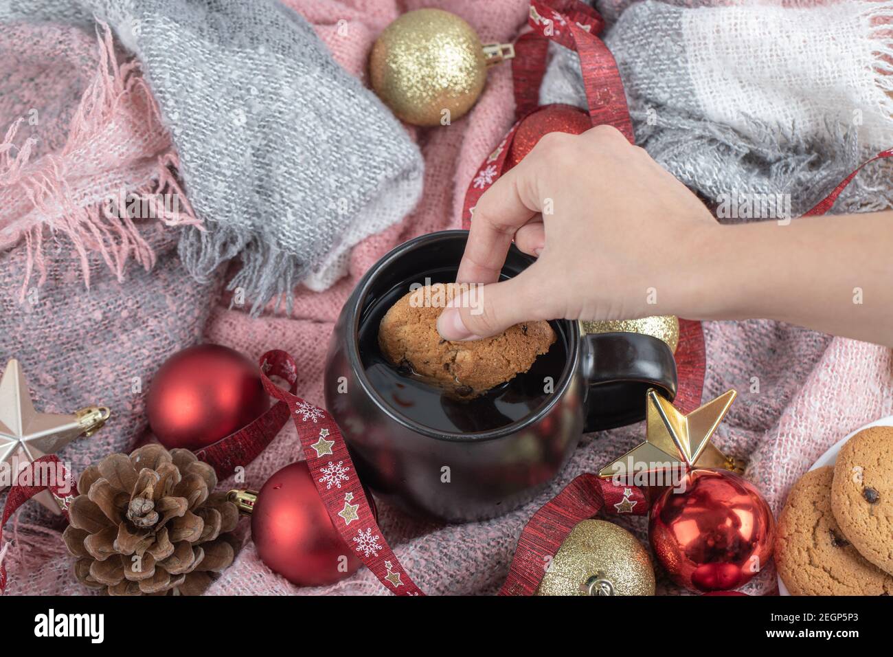 Sumergir la galleta de jengibre en la bebida en la mesa cubierta con adornos de navidad Foto de stock