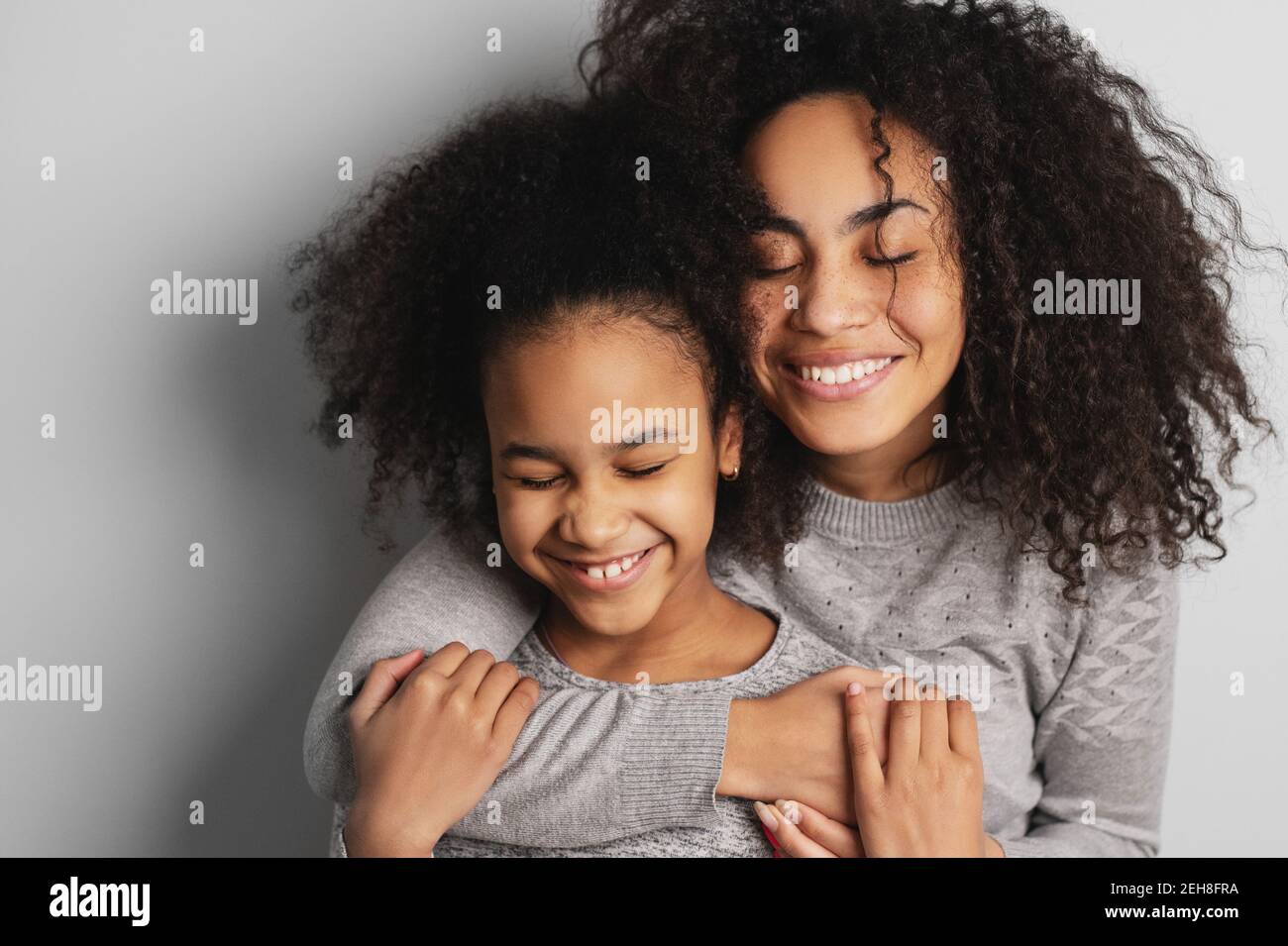Feliz mamá afroamericana y su linda hija sonriendo y abrazando con los ojos cerrados. Foto de stock