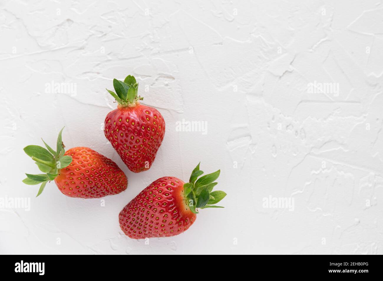 Tres fresas rojas frescas del Jardín sobre Blanco Texturizada Antecedentes Foto de stock