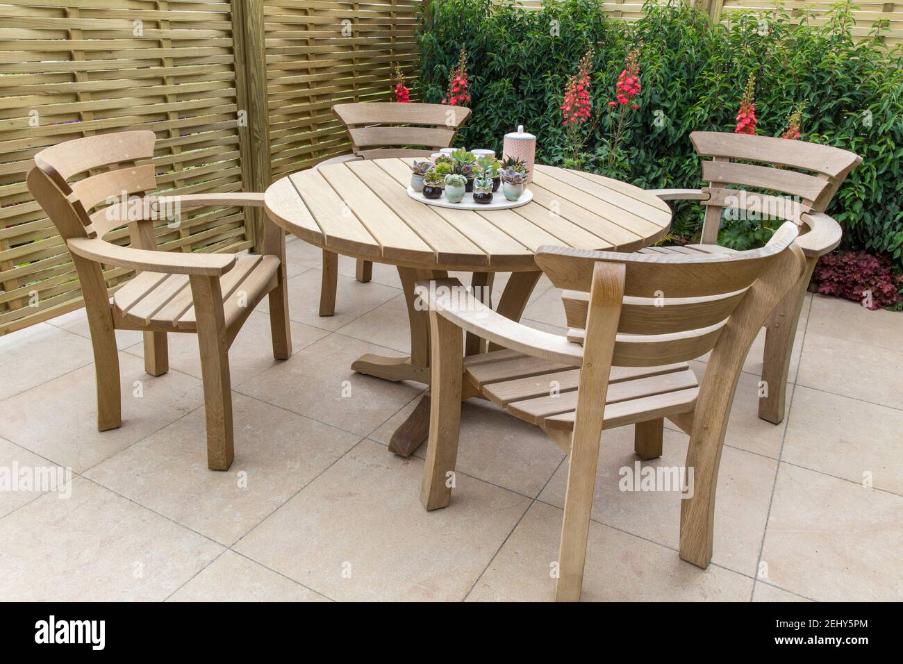 Zona de muebles de comedor exterior Moderno patio pavimentado de piedra -  muebles de jardín de madera dura mesa y sillas muestran plantas suculentas  en ollas de cerámica Reino Unido Fotografía de