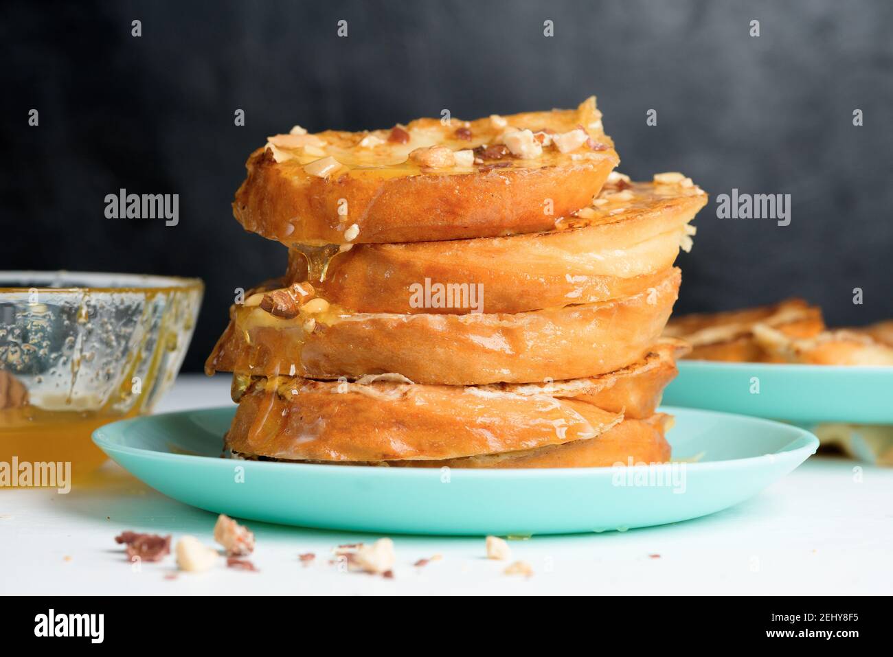 Pan francés casero frito con miel y frutos secos sobre un plato azul sobre  un fondo oscuro. Empapado en mezcla de huevo de leche. Desayuno saludable.  Primer plano Fotografía de stock -