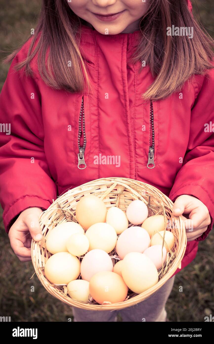 Niña pequeña con chaqueta roja, sosteniendo una cesta de huevos. Pascua,  símbolo de primavera, disparo vertical Fotografía de stock - Alamy