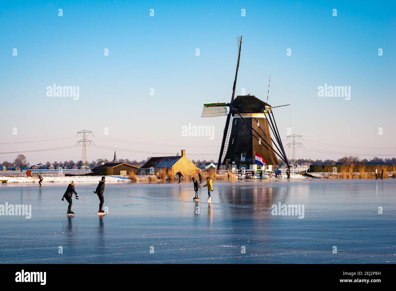 Escena clásica holandesa con patinadores de hielo en un molino de viento tradicional durante un período frío en invierno. Foto de stock