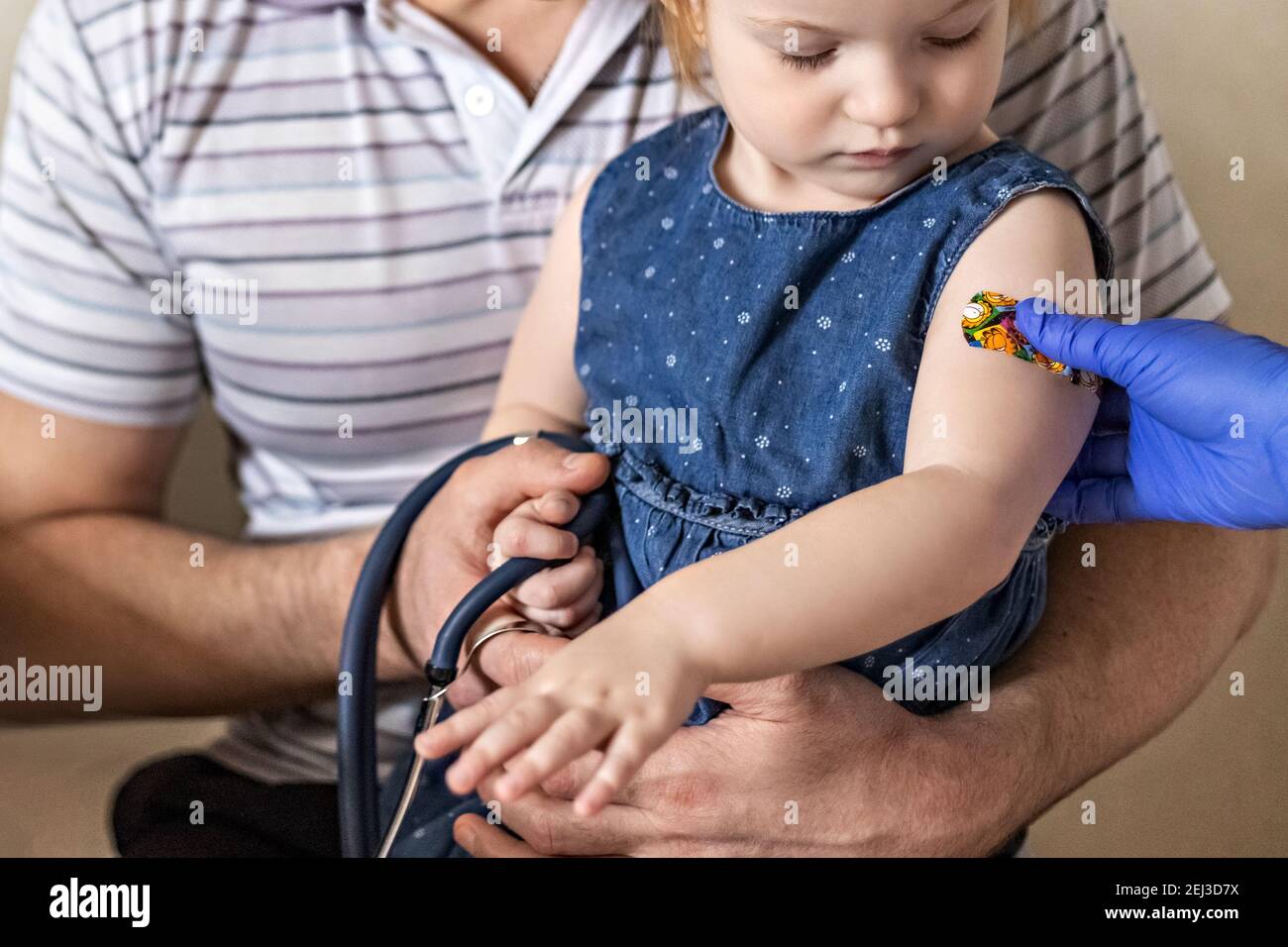 Vacunación de una niña en los brazos de su padre en el consultorio del médico desde el coronavirus. El divertido yeso adhesivo de los niños. Vacuna contra el covid-1 Foto de stock