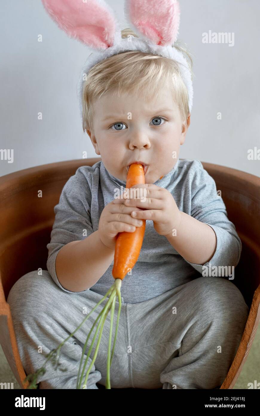 Lindo niño pequeño en orejas de conejo masticando en un zanahoria Foto de stock