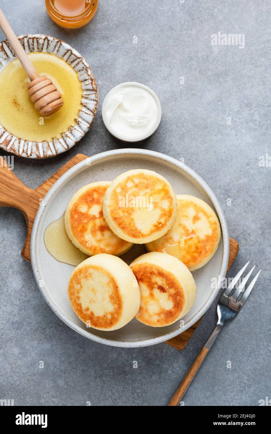 Fritters de queso cottage Sirniki servido con miel y crema agria sobre fondo de hormigón gris, vista superior Foto de stock
