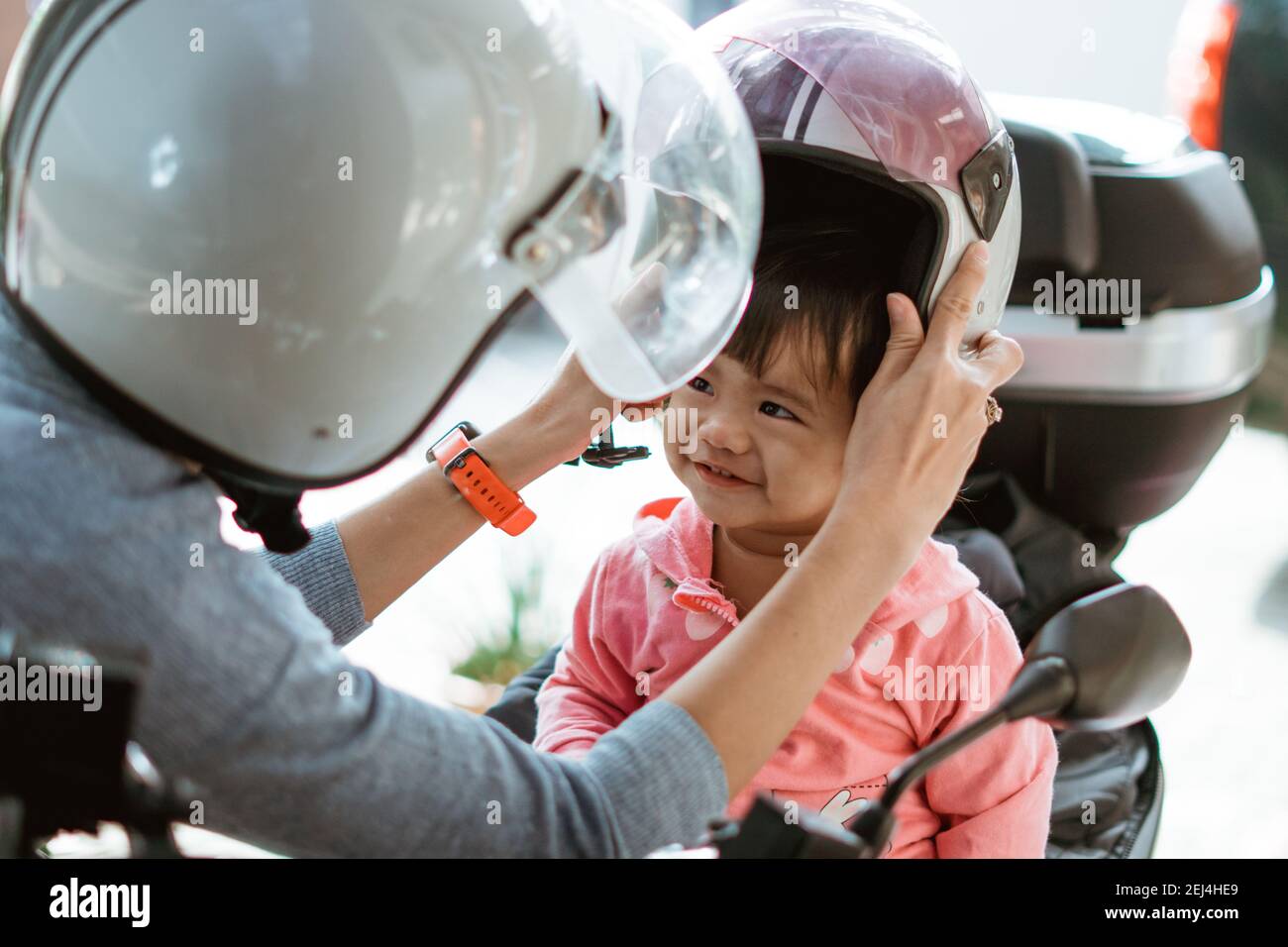 el bebé usa un casco para motocicleta cuando la madre ayuda él en la moto  Fotografía de stock - Alamy